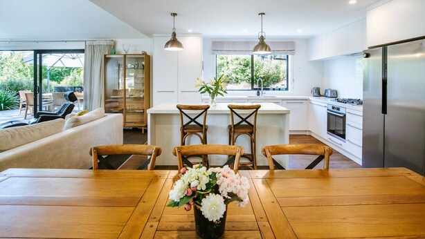 Een moderne keuken met een eethoek, houten stoelen, een tafel met een bloevas en uitzicht op de natuur.