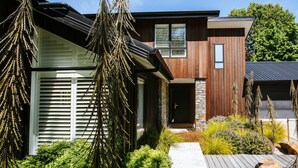 Een modern herenhuis met twee verdiepingen, een gevel van natuursteen, een houten buitenkant en een verzorgde tuin met diverse planten en een houten terras.