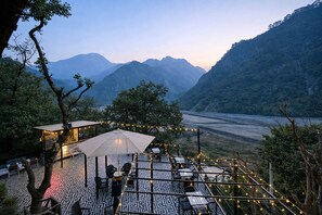 An outdoor terrace with patterned flooring, tables, chairs, and string lights. - Riverline Gold Resort (Yamkeshwar)