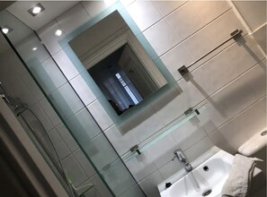 Une salle de bain avec un miroir encadré de verre, un lavabo blanc, une douchette à main et un porte-serviettes.