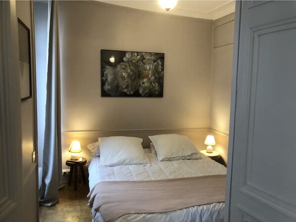 Une chambre à coucher avec un lit, deux lampes de chevet, un tableau au mur et une porte.