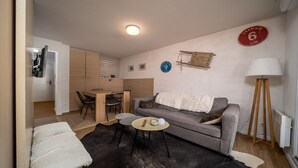 Ein kompakter Wohnbereich mit Sofa, einem kleinen runden Tisch, einer Stehlampe und einer Küchenzeile.