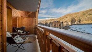 Ein Holzbalkon mit Blick auf schneebedeckte Berge und ein Gebäude in der Ferne.
