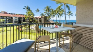 A balcony with a table and chairs, overlooking a pool and palm trees, with buildings in the background.