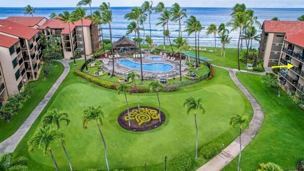 A resort with a central pool, palm trees, and a view of the ocean.