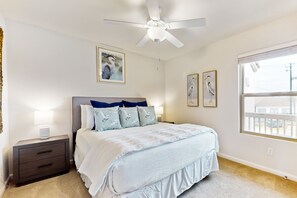 A bedroom with a bed, a nightstand, a ceiling fan, and a window.