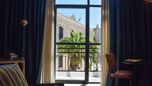 Una habitación con un ventanal grande, una silla, una mesita y un cojín a rayas.