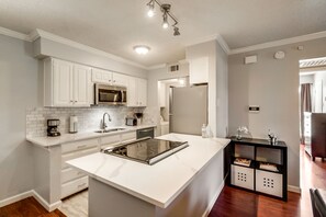 A modern kitchen with white cabinetry, a built-in microwave, a stainless steel refrigerator, and a central island with a stovetop.