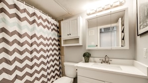 Un baño con lavamanos blanco, espejo y cortina de ducha con estampado de zigzag.