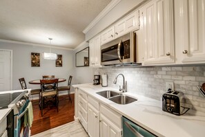 A modern kitchen with white cabinetry, stainless steel appliances, a dining area with a round table and chairs, and a tiled backsplash.