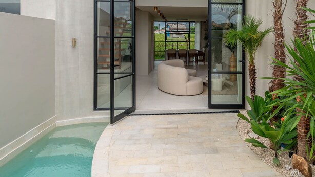 A modern house with a glass door leading to a patio area with a pool and outdoor seating. - Vesna Townhouse 7  (Canggu)