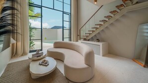 A modern living room with a curved sofa, a round coffee table, and a staircase with wooden steps. - Vesna Townhouse 7  (Canggu)