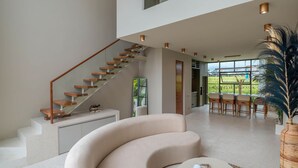 A spacious living area with a curved sofa, a round coffee table, and a staircase leading to an upper level. - Vesna Townhouse 7  (Canggu)