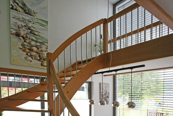 Una escalera de madera con vistas a un cuadro de playa y una lámpara colgante.