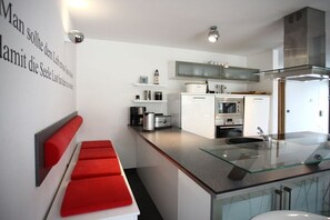 Una cocina moderna con armarios blancos, una campana extractora de acero inoxidable y una isla de vidrio con un fregadero.