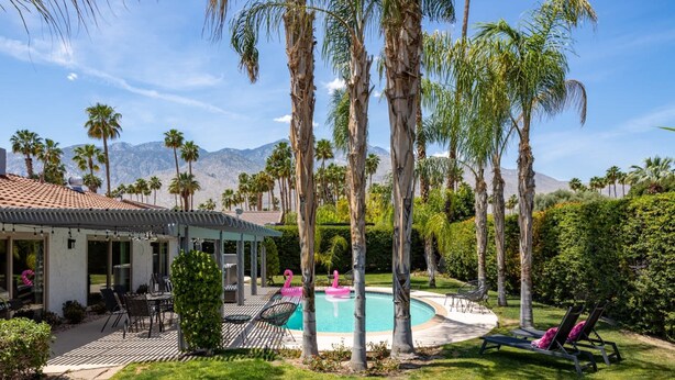 Un área de piscina con sillones de descanso, una pérgola y palmeras.