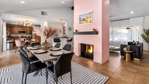 Una sala de estar moderna con chimenea, comedor y cocina al fondo.