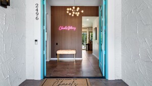 Una entrada moderna con un letrero de neón que dice "Chanel's Getaway", un banco y un felpudo.