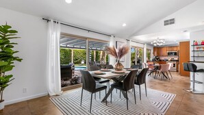 Un comedor amplio con una gran mesa, sillas y vistas a una piscina y follaje exterior.