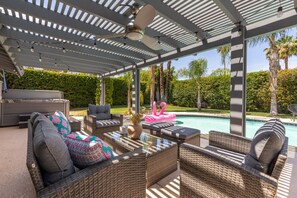 Uma área de pátio ao ar livre com móveis de vime, piscina e pérgola.