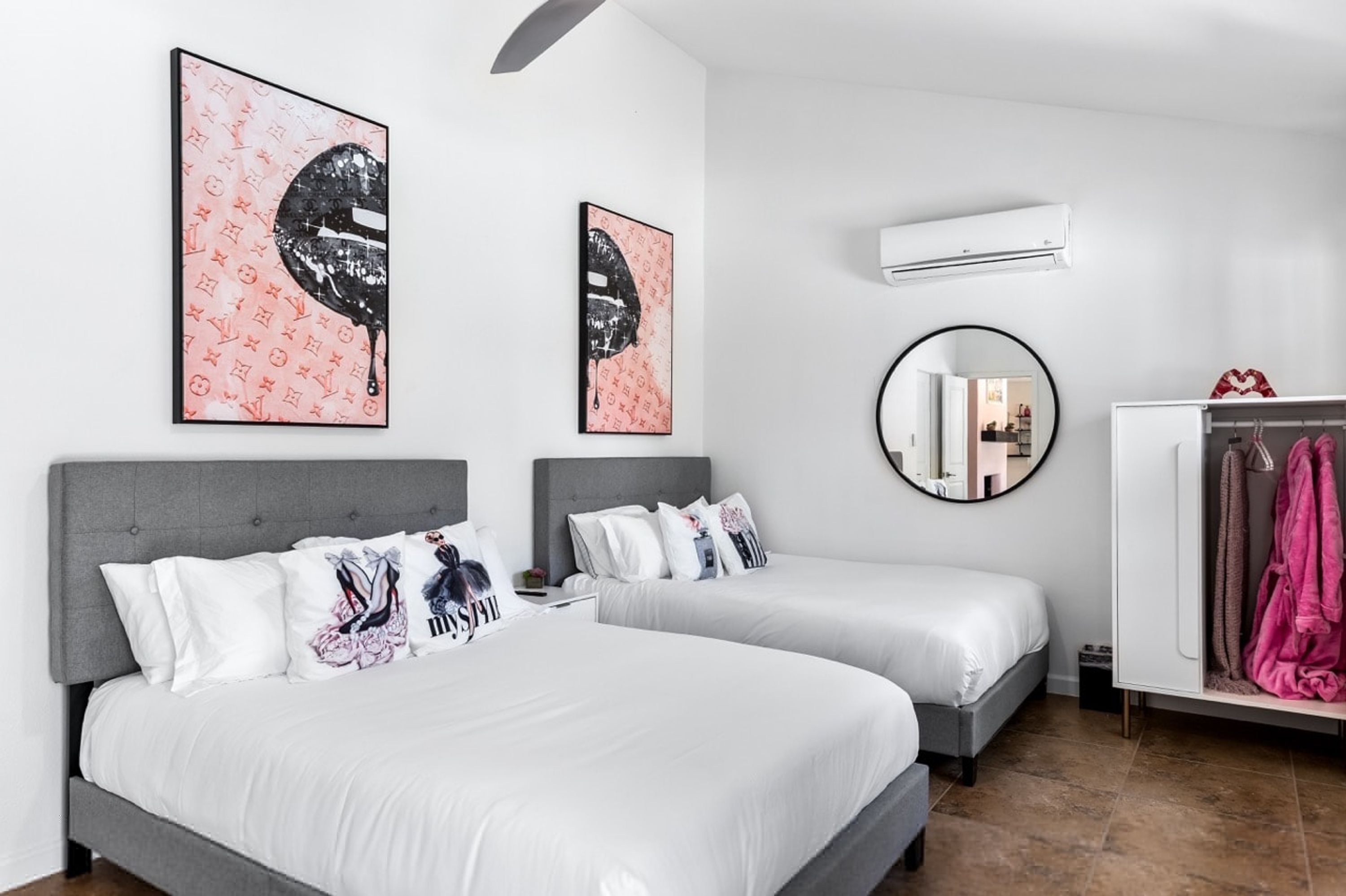 A hotel room with two beds, a wardrobe, a round mirror, and artwork on the walls.