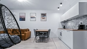 A modern kitchen with white cabinets, a wooden countertop, and a hanging chair. - RentPlanet - Apartament Muranów (Warsaw)