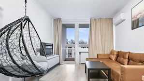 A modern living room with a hanging chair, a sofa, a coffee table, and a view through a glass door to an outdoor balcony. - RentPlanet - Apartament Muranów (Warsaw)
