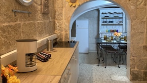A kitchen with stone walls, a coffee maker, a refrigerator, and a dining area with a table and chairs. - Charming Central Townhouse in Sliema  (Sliema)