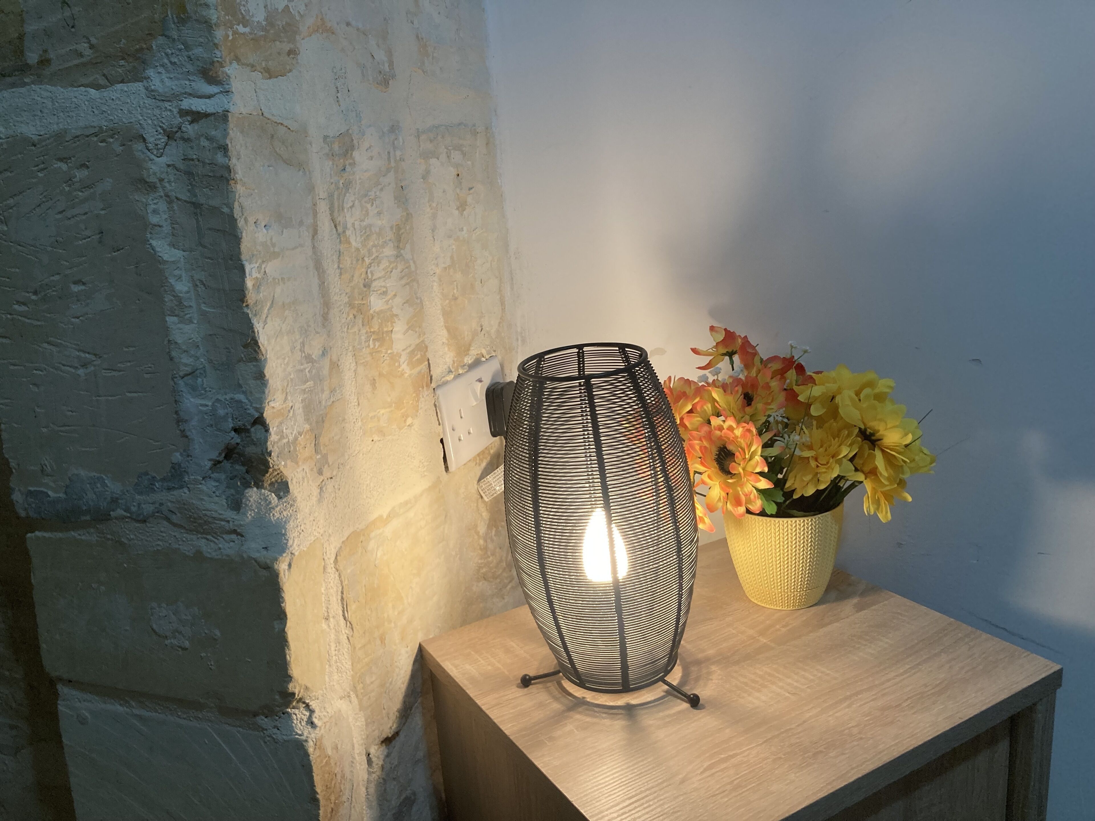 A wall-mounted light fixture on a wooden surface next to a wall with a rough texture.