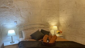 A bedroom with a stone wall, a metal bed frame, a bedside table with a lamp, and a nightstand with a lamp. - Charming Central Townhouse in Sliema  (Sliema)