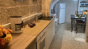 A kitchen with a stone wall, a clock, a coffee maker, and a table with chairs. - Charming Central Townhouse in Sliema  (Sliema)
