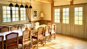 Un espace repas comprenant une table et des chaises en bois, de grandes fenêtres et un plafond avec des poutres apparentes.