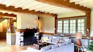 Un salon chaleureux avec une cheminée, un canapé, un coin repas et une grande fenêtre donnant sur un paysage verdoyant.