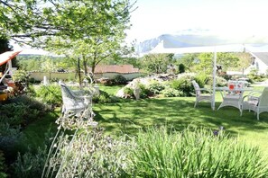 A garden with a white umbrella, outdoor furniture, and a mountain view.