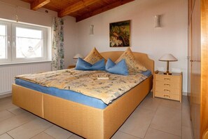 A bedroom with a bed, a nightstand, a lamp, a window, and a painting on the wall.
