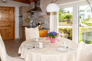 A dining area with a round table set for four, a kitchen in the background, and a view of the outside.