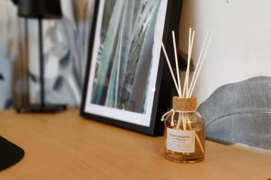 A small bottle of pomegranate and orange essential oil with reed diffusers on a wooden table.