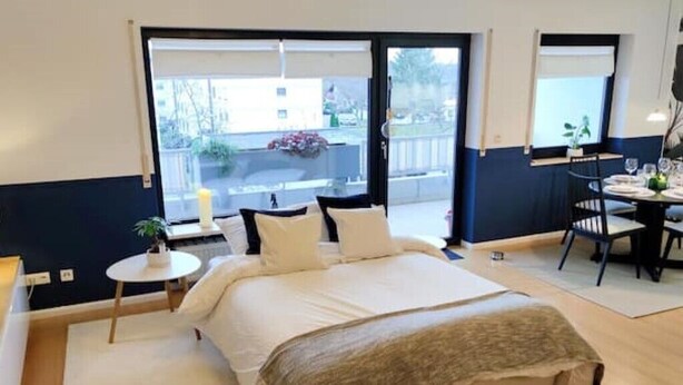 Ein Schlafzimmer mit Bett, einem kleinen Tisch mit Pflanze und einem Fenster mit Blick nach draußen.