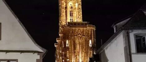 A tall, illuminated tower with intricate architectural details, surrounded by buildings with white facades.