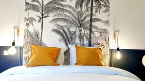 Ein Hotelzimmer mit einem Bett, zwei gelben Kissen, einer weißen Daunendecke und einer Wandteppich-Motiv von Palmen.