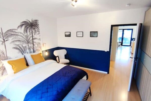 Un dormitorio con una cama, una silla y un escritorio. Hay tres cuadros en la pared.