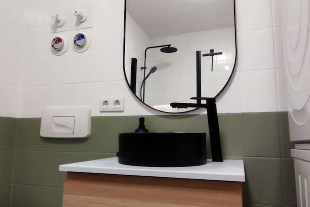 Un bany amb un lavabo blanc, un aixeta negra i un mirall. Hi ha dos interruptors de llum fixats a la paret i una presa elèctrica blanca.