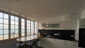 Eine moderne Küche mit einem großen Fenster mit Meerblick, einem Essbereich mit Hockern und einer schwarzen Arbeitsplatte.