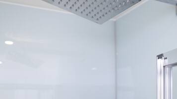 A modern bathroom with a glass shower enclosure, a black shelf, and a white wall.