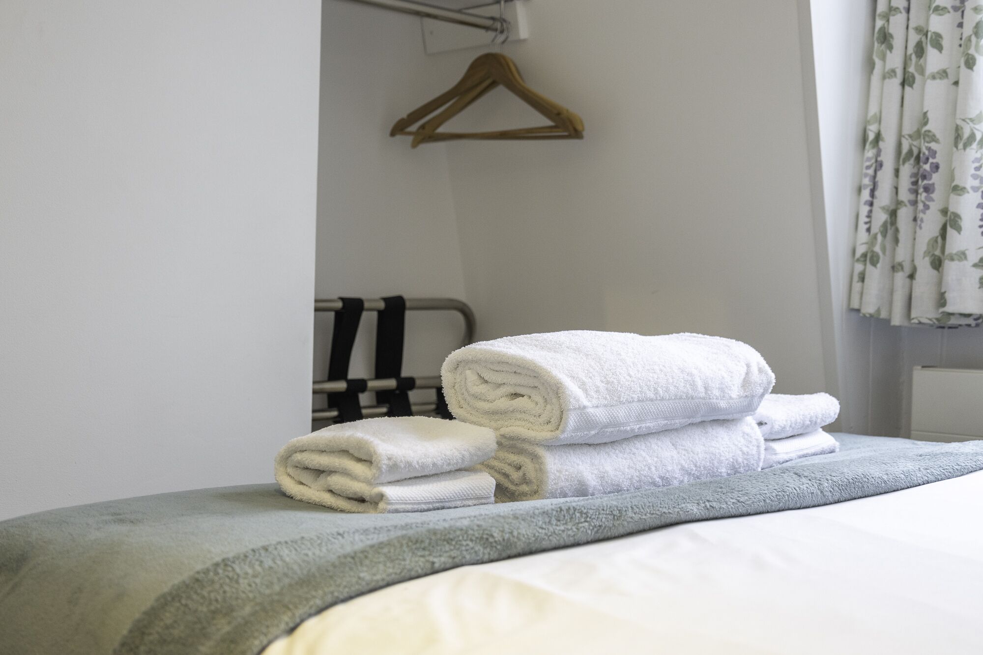 A neatly made bed with rolled white towels and a grey blanket.