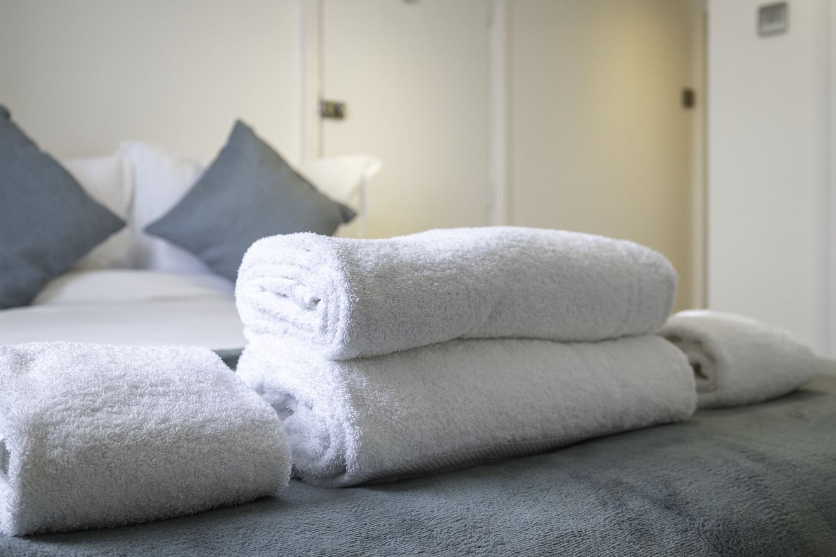 Una cama bien hecha con almohadas y una pila de toallas dobladas.