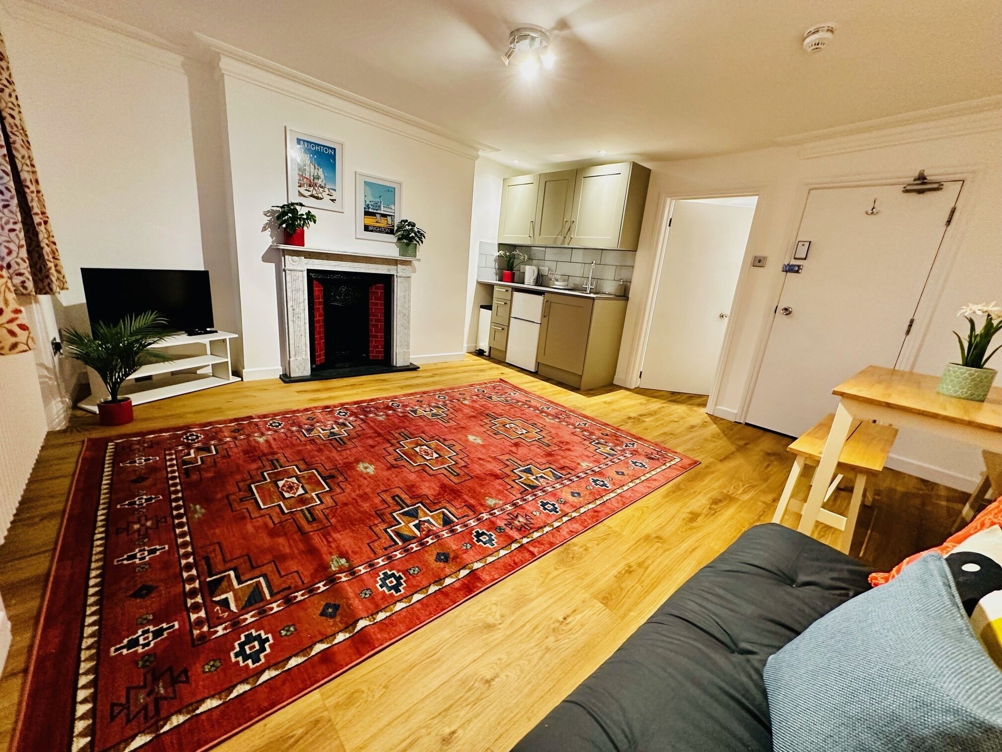 Ein Wohnzimmer mit einem roten, gemusterten Teppich, einem Kamin, einem Fernseher und einer Küchenzeile mit Schränken und einer Arbeitsplatte.