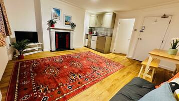 Ein Wohnzimmer mit einem roten, gemusterten Teppich, einem Kamin, einem Fernseher und einer Küchenzeile mit Schränken und einer Arbeitsplatte.