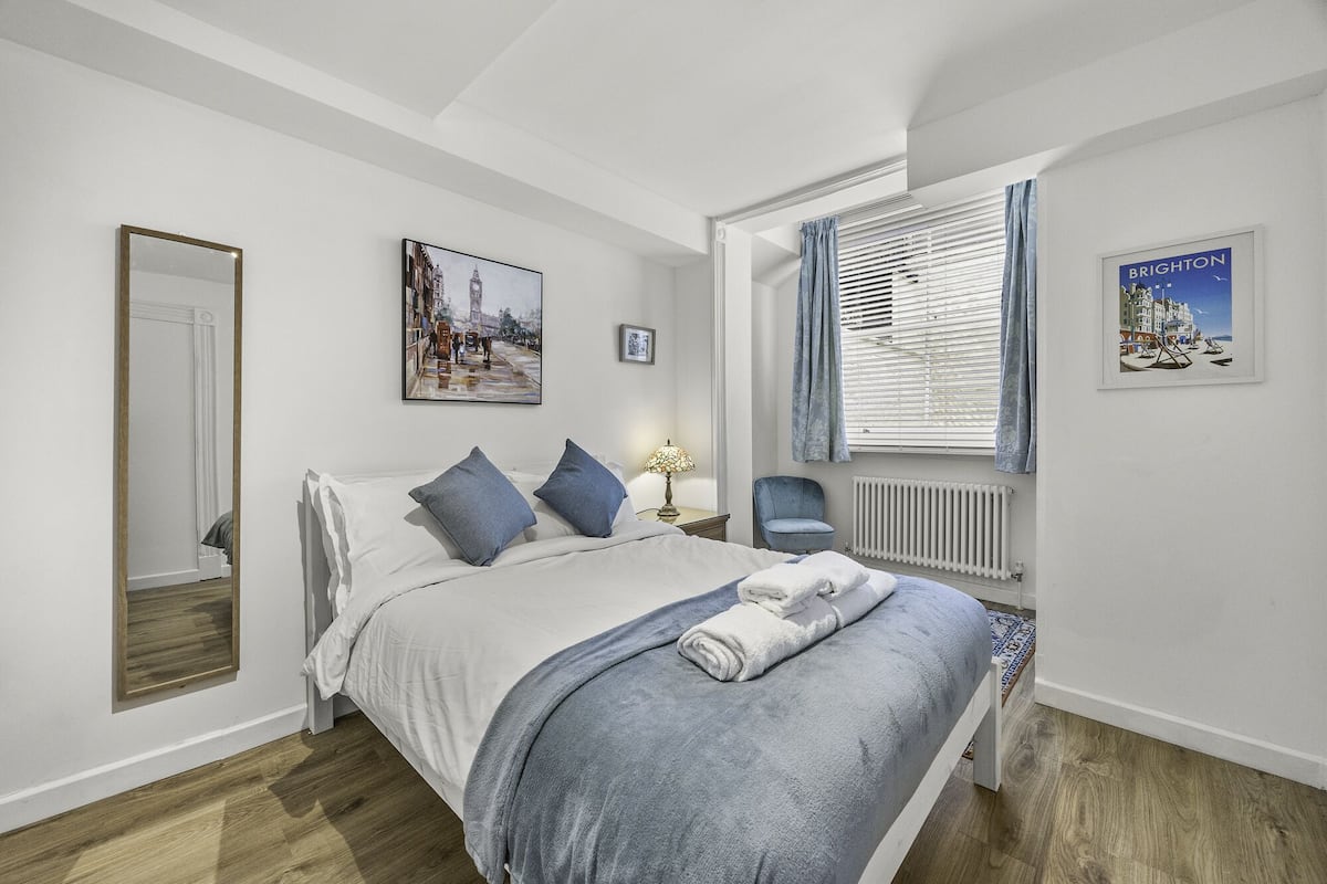 Un dormitorio con una cama, una silla, un radiador y dos cuadros en la pared.