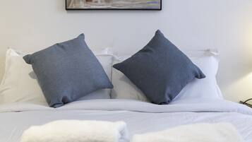 Una cama bien hecha con sábanas blancas y dos almohadas grises.